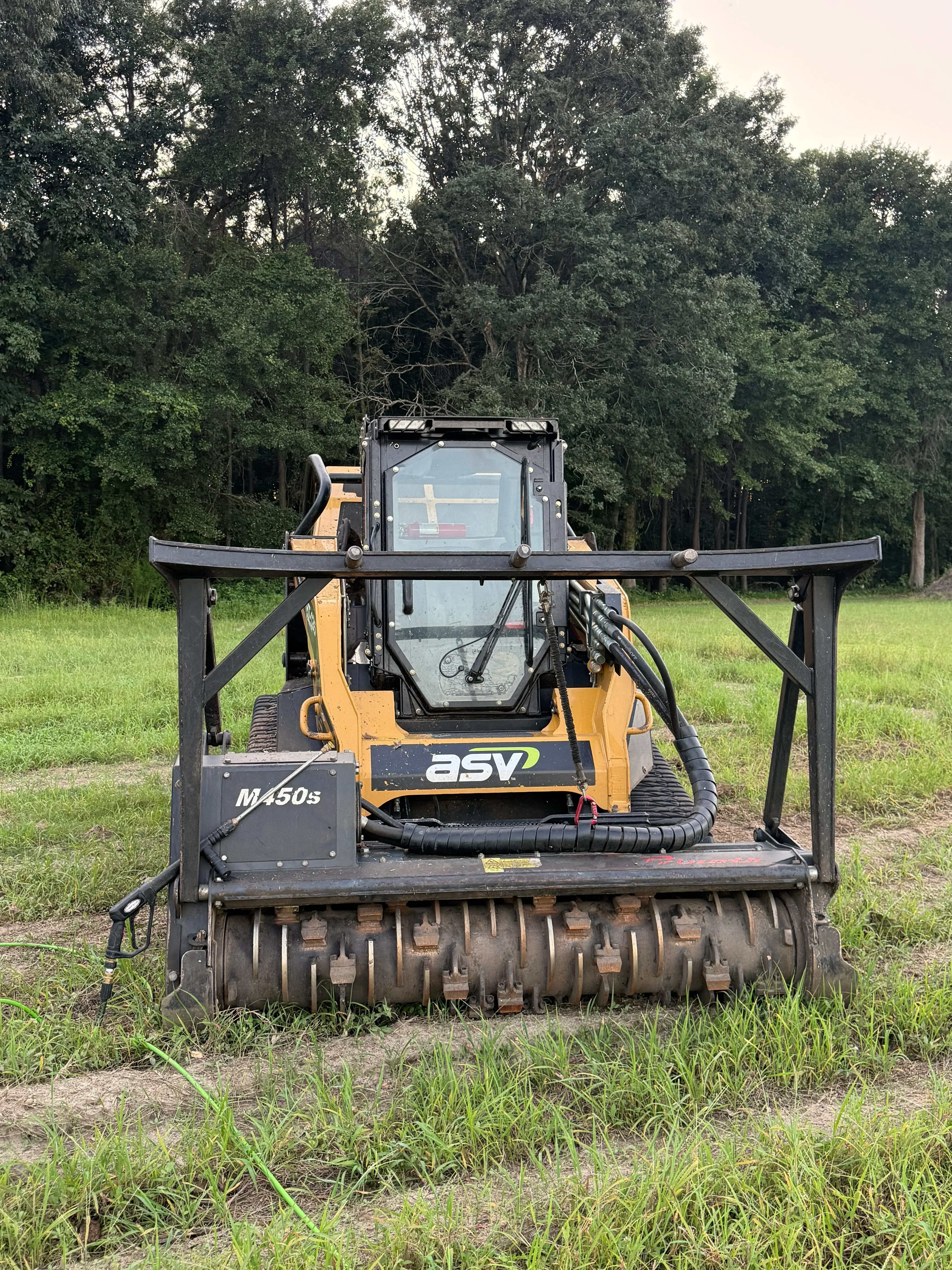 Tracked excavator with hydraulic mulcher attachment clearing trees and brush