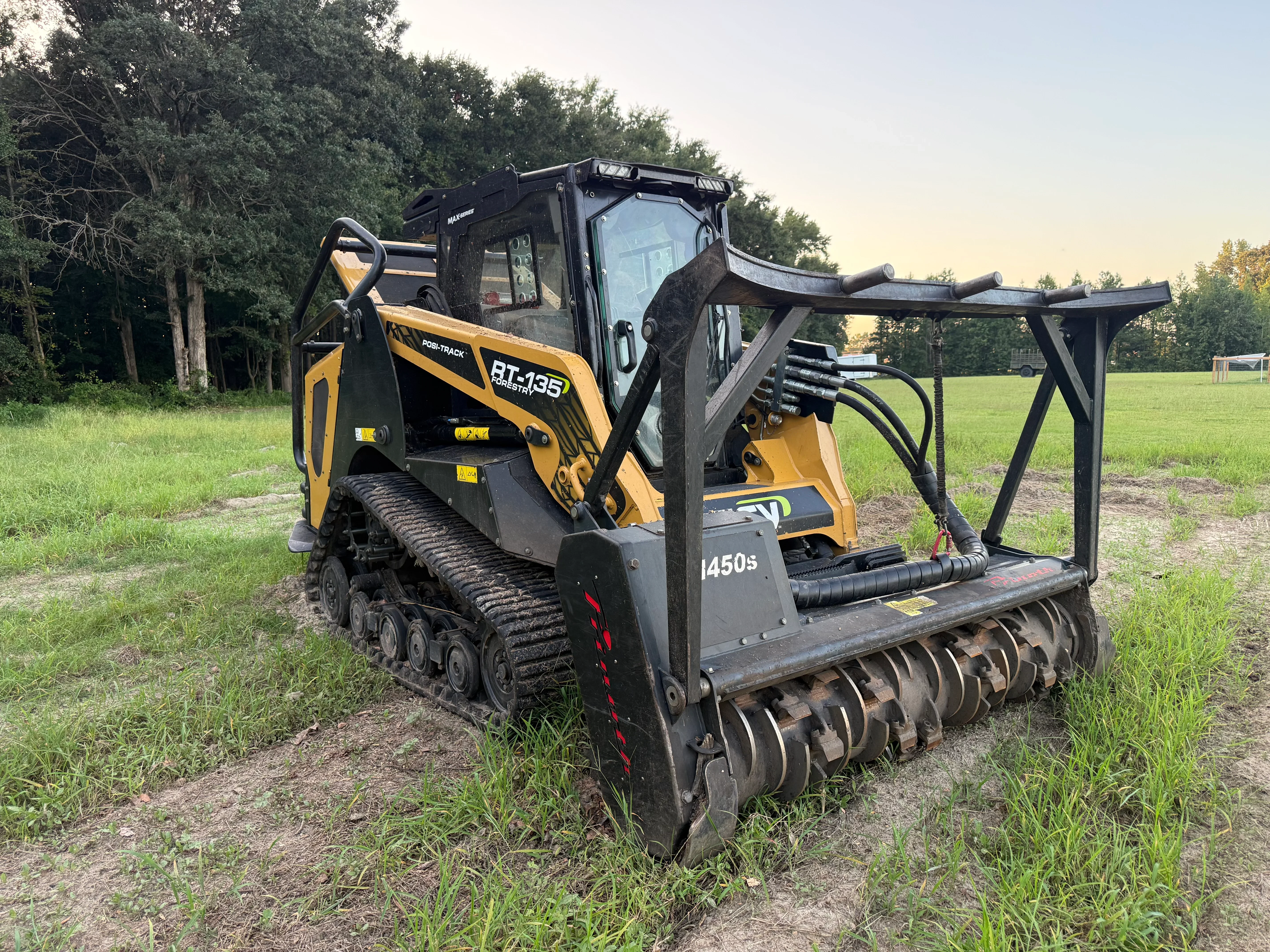 Compact track loader with forestry mulching head attachment clearing overgrown vegetation