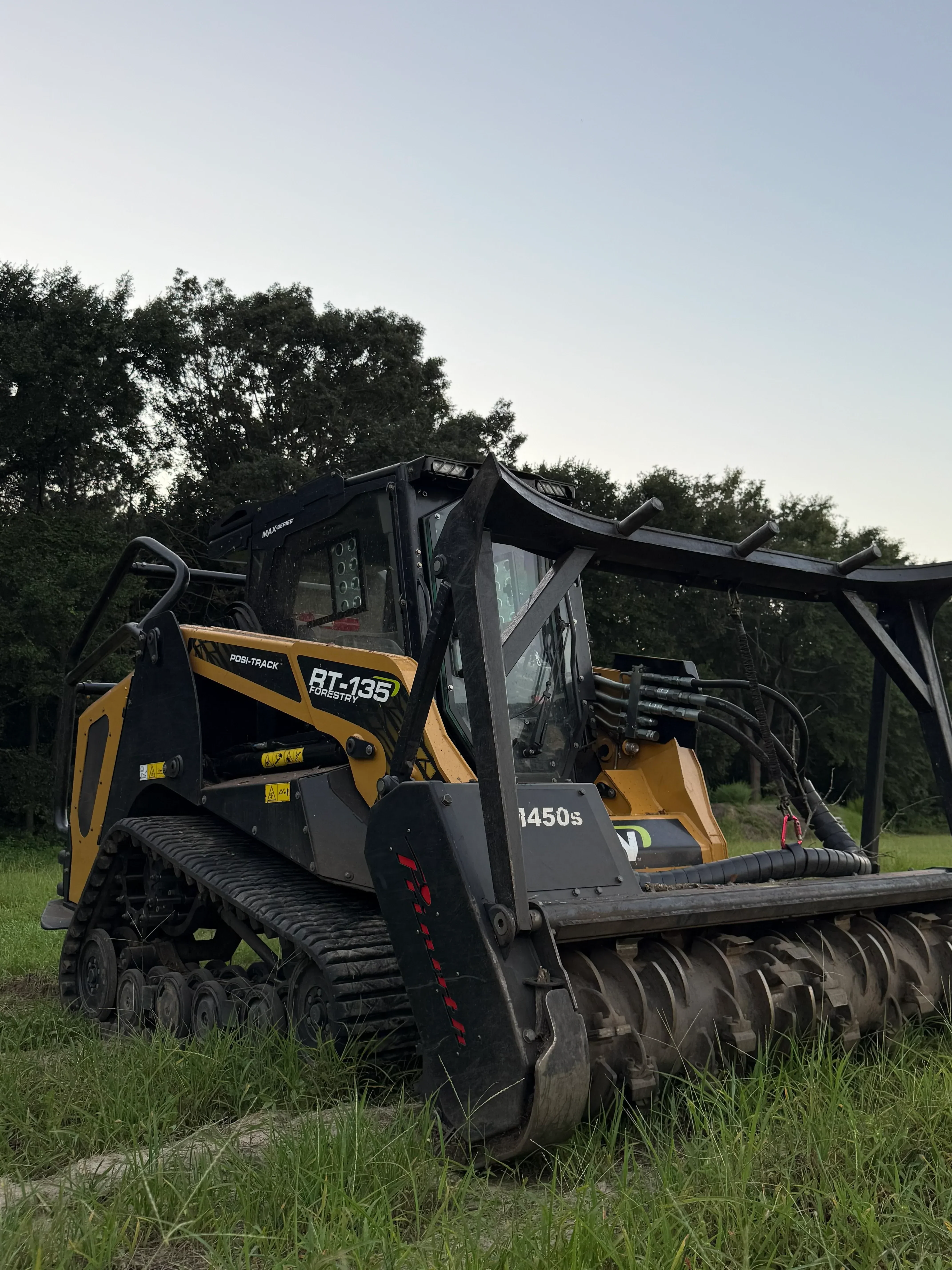 Tracked forestry mulcher with hydraulic head clearing vegetation on grassy terrain